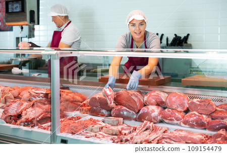 Young female seller shows demonstrates raw beef ribs in glass showcase of refrigerator. Young female seller shows demonstrates raw beef ribs in glass showcase of refrigerator. 109154479