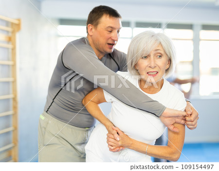 Trainer and mature woman train painful hold on self-defense course in sport gym 109154497