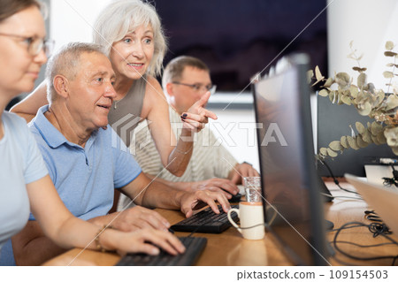 Elderly people help each other learn how to use computer. Positive woman suggests right decision to an mature man 109154503