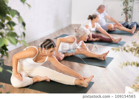 Elderly women together with a young coach doing stretching and doing yoga on mats in gym 109154565