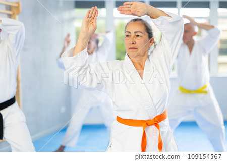 Old woman attendee of karate classes practicing kata standing in row with others Old woman attendee of karate classes practicing kata standing in row with others 109154567