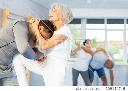Trainer and mature woman train painful hold on self-defense course in sport gym 109154746