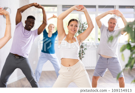 Young female dance instructor conducting warm-up with group of mature people 109154913