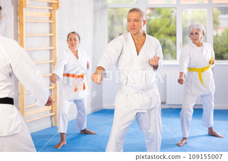 Old man attendee of karate classes practicing kata standing in row with others 109155007