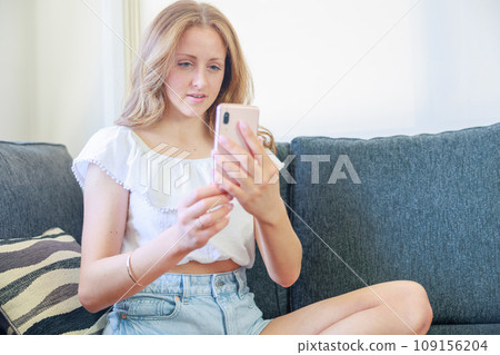 坐在沙發上操作智慧型手機的白人女性（微笑） 109156204