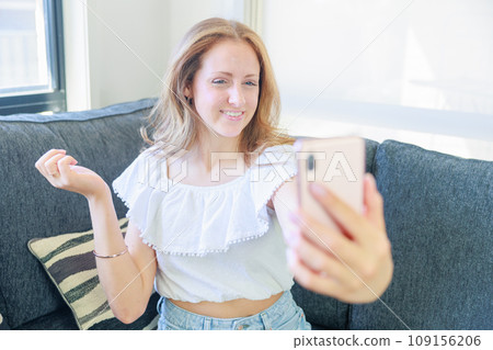 Caucasian girl sitting on the sofa and taking a selfie Caucasian girl sitting on the sofa and taking a selfie 109156206