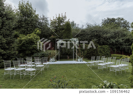 Beautiful wedding arch decorated with flowers and chairs for guests Beautiful wedding arch decorated with flowers and chairs for guests 109156462