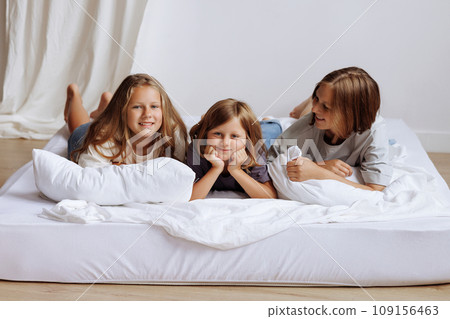 Sisters lying on a bed in their home smmiling for the camera. 109156463