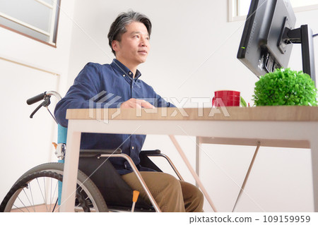 Middle-aged man in a wheelchair staring at a PC display Middle-aged man in a wheelchair staring at a PC display 109159959