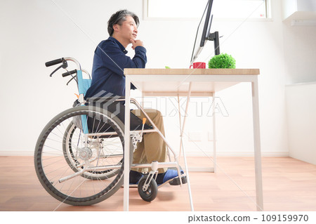 Middle-aged man in a wheelchair staring at a PC display Middle-aged man in a wheelchair staring at a PC display 109159970