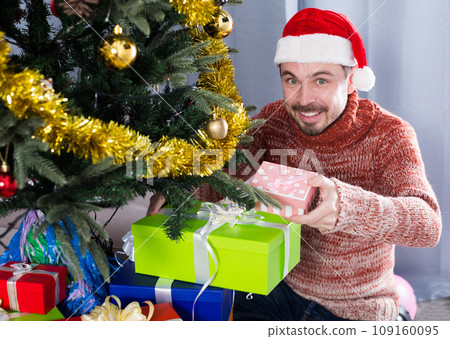 Man wearing Santa puts gifts under the Christmas tree 109160095