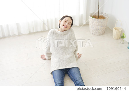 A woman relaxing while sitting on the wooden floor in the living room A woman relaxing while sitting on the wooden floor in the living room 109160344