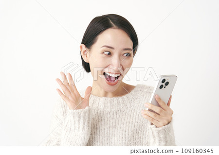 A middle-aged woman looking at her smartphone and smiling, surprised, white background 109160345