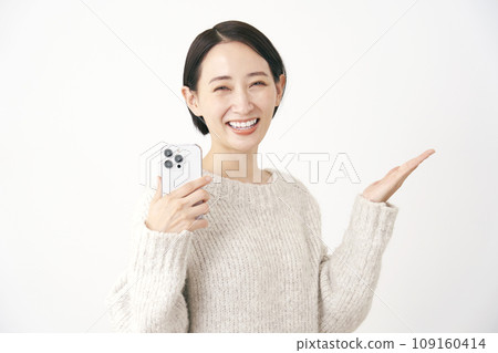 中年婦女拿著智慧型手機，用手掌、白色背景指著右側 109160414