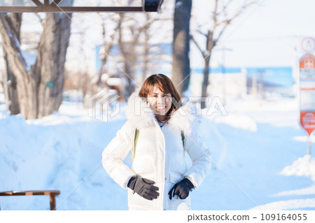happy Traveler with Sweater and backpack walking on snow covered road in frosty weather, woman tourist sightseeing in Sapporo city, Hokkaido, Japan Winter Travel and Vacation concept 109164055