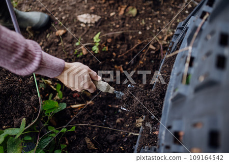 Girl removing compost from a composter in the garden. Concept of composting and sustainable organic gardening. 109164542