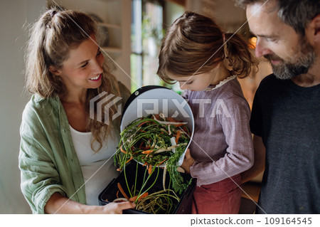 Girl helping parents put kitchen waste, peel and leftover vegetables scraps into kitchen compostable waste. Concept of composting kitchen biodegradable waste. 109164545