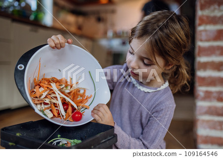 Girl putting kitchen waste, peel and leftover vegetables scraps into kitchen compostable waste. Concept of composting kitchen biodegradable waste. 109164546