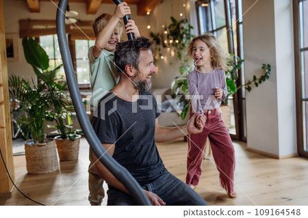Father and kids cleaning house, vacuuming the floors with a vacuum cleaner. Young boy and girl helping with house chores. 109164548