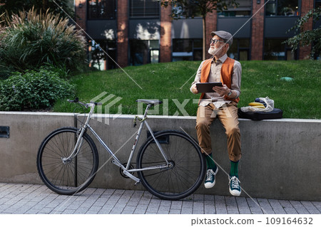 Stylish senior man sitting in the city park, holding tablet, shopping online. Concept of digital literacy and seniors using digital technologies. Stylish senior man sitting in the city park, holding tablet, shopping online. Concept of digital literacy and seniors using digital technologies. 109164632