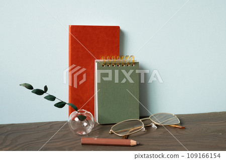 Office desk with diary note, eyeglasses, pencil, plant on wooden table. blue wall background 109166154