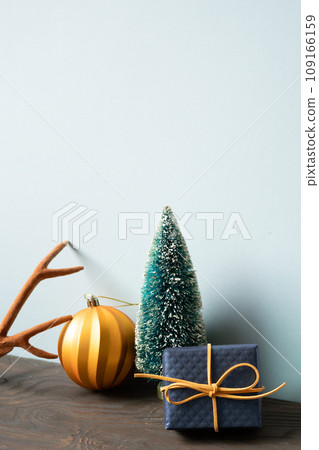 Christmas decoration ornament fir tree, golden ball, deer antler, gift box on wooden table. blue wall background Christmas decoration ornament fir tree, golden ball, deer antler, gift box on wooden table. blue wall background 109166159