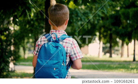 Tired schoolboy proceeds to educational institution on sunny day. Schoolboy walks on familiar path to place of learning. Schoolboy with backpack on shoulders carries school supplies on way to school 109168261