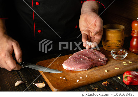 The cook adds coarse salt to the meat steak. The process of cooking beef meat or shish kebab on the kitchen table with spices and garlic 109168453