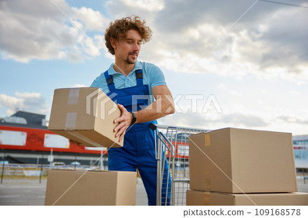 Deliveryman stacking parcel boxes into trolley cart providing courier service 109168578