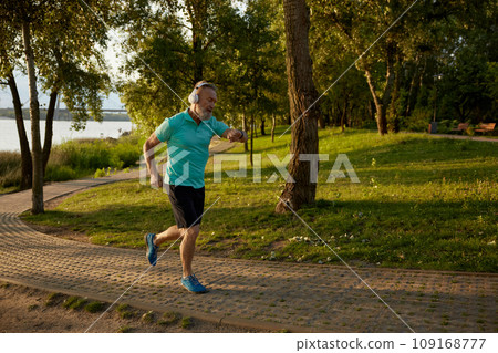 Senior man wearing headset looking at wristwatch running in park Senior man wearing headset looking at wristwatch running in park 109168777