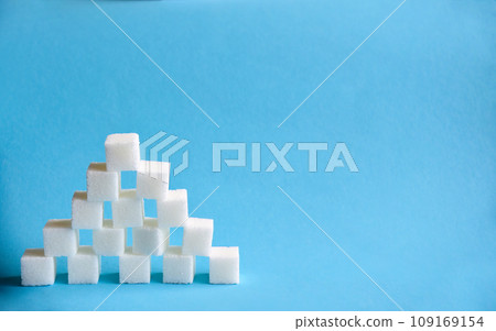Pyramid made from cubes of refined white sugar on blue background. Copy space Pyramid made from cubes of refined white sugar on blue background. Copy space 109169154