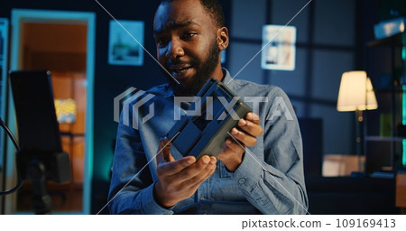 African american content creator filming video review of newly launched portable V mount battery, unboxing it and presenting to audience. Media star recording unboxing of charging device for viewers 109169413