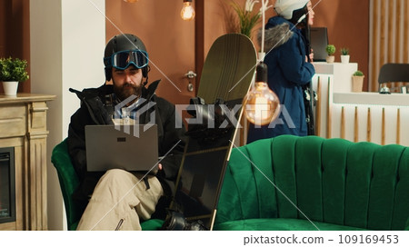 Male tourist works on laptop before starting skiing session down alpine slopes, searching for reviews and places at exclusive mountain resort. Equipped man using modern gadget. Male tourist works on laptop before starting skiing session down alpine slopes, searching for reviews and places at exclusive mountain resort. Equipped man using modern gadget. 109169453
