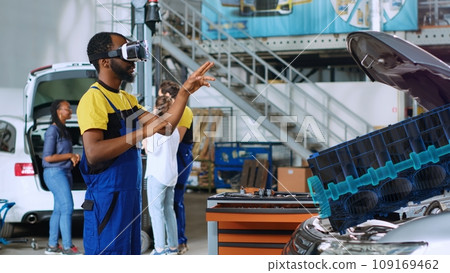 Repairman in car service using advanced virtual reality technology to visualize engine turbine in order to fix it. Knowledgeable garage specialist wearing vr glasses while servicing defective vehicle Repairman in car service using advanced virtual reality technology to visualize engine turbine in order to fix it. Knowledgeable garage specialist wearing vr glasses while servicing defective vehicle 109169462