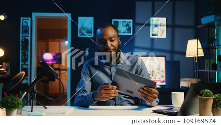 BIPOC content creator filming technology review of newly launched tablet, unpacking it and presenting specifications to audience. Internet star showing digital device to viewers 109169574