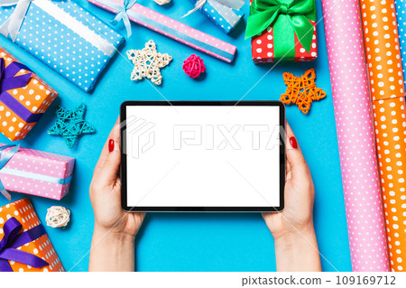 Top view of woman holding tablet in her hands on blue background made of Christmas decorations. New Year holiday concept. Mockup Top view of woman holding tablet in her hands on blue background made of Christmas decorations. New Year holiday concept. Mockup 109169712