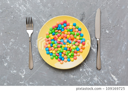 cutlery on table and sweet plate of candy. Health and obesity concept, top view on colored background cutlery on table and sweet plate of candy. Health and obesity concept, top view on colored background 109169725