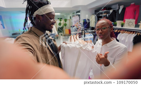 Content creator and employee browsing through wares in thrift shop with vintage clothes, presenting hidden gems. Influencer showcasing premium second hand clothing store high street garments 109170050