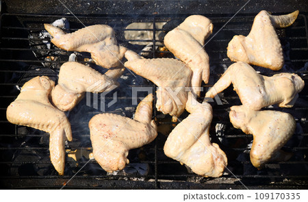 Raw chicken wings marinated in sour cream and spices, grilling on the grill grate. Start cooking, barbecue Raw chicken wings marinated in sour cream and spices, grilling on the grill grate. Start cooking, barbecue 109170335