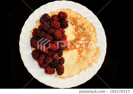 Ripe blackberries on ruddy appetizing pancake on white glass plate and black table 109170557