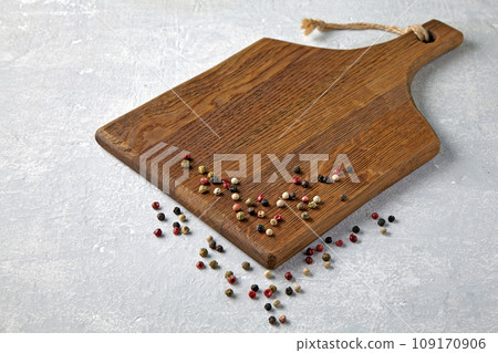 Brown wooden cutting board with scattered multi-colored peppercorns on a gray stone table Brown wooden cutting board with scattered multi-colored peppercorns on a gray stone table 109170906
