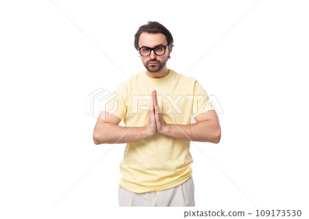 young handsome european brunette guy with a beard and mustache in glasses folded his hands together young handsome european brunette guy with a beard and mustache in glasses folded his hands together 109173530