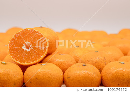 There is half a mandarin orange with a cross section visible on top of a spread of mandarin oranges. 109174352