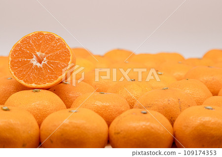 There is half a mandarin orange with a cross section visible on top of a spread of mandarin oranges. There is half a mandarin orange with a cross section visible on top of a spread of mandarin oranges. 109174353