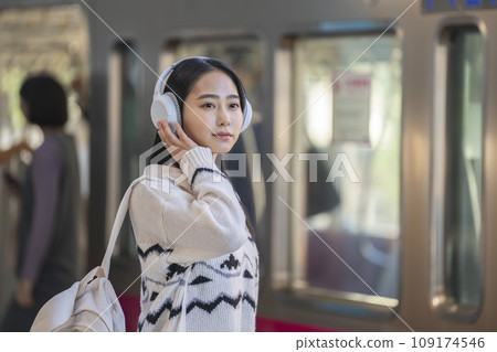 一位戴著耳機的年輕女子在月台等待火車。攝影由京王電鐵株式會社提供。 109174546