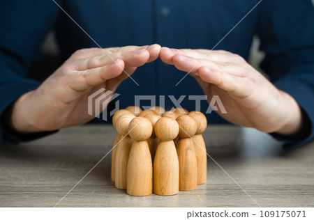A man covers a group of people figures with house roof gesture. The concept of insurance and social protection. Life insurance. Customer care. Human resources. 109175071