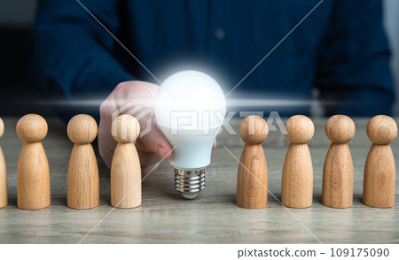 A man inserts a glowing light bulb idea between people. Inspire society to new ideas. Teamwork brainstorming. Research and development. Enlightenment and education. Ideology, paradigm 109175090