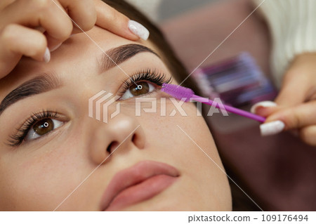 master combs the eyelashes of the client after the eyelash extension procedure. close-up. Cosmetology and skin care 109176494