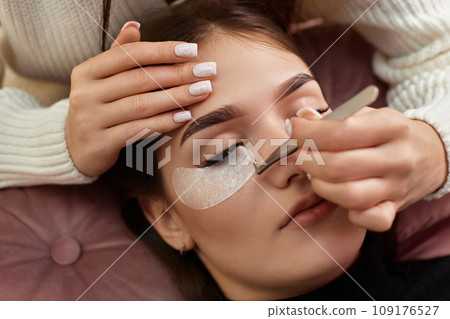 cosmetologist removes glue cotton tape under eye. Eyelash extension procedure cosmetologist removes glue cotton tape under eye. Eyelash extension procedure 109176527
