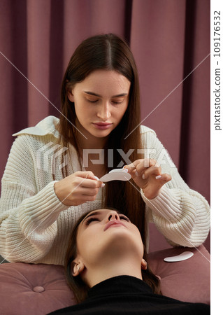cosmetologist preparing glue ribbon under eye. Eyelash extension procedure cosmetologist preparing glue ribbon under eye. Eyelash extension procedure 109176532